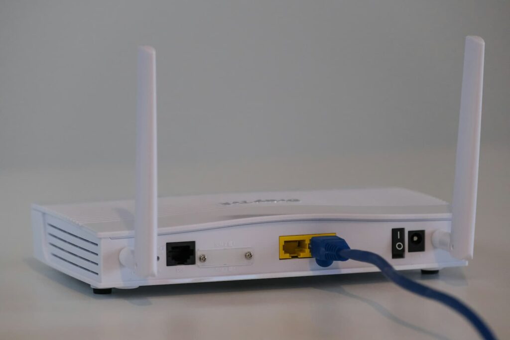 De achterkant van een witte wifi-router met twee antennes, waarop een blauwe ethernetkabel is aangesloten.